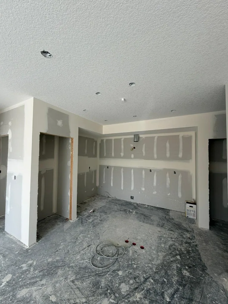 Worker installing drywall near ceiling with framing and insulation visible